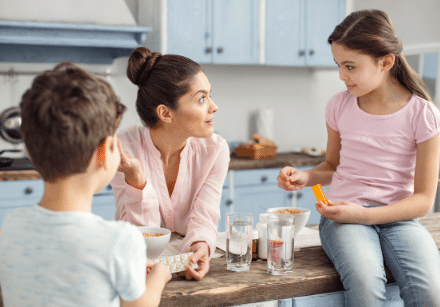 Stay at home mom standing in kitchen with one child sitting on counter and one standing near counter talking about working from home