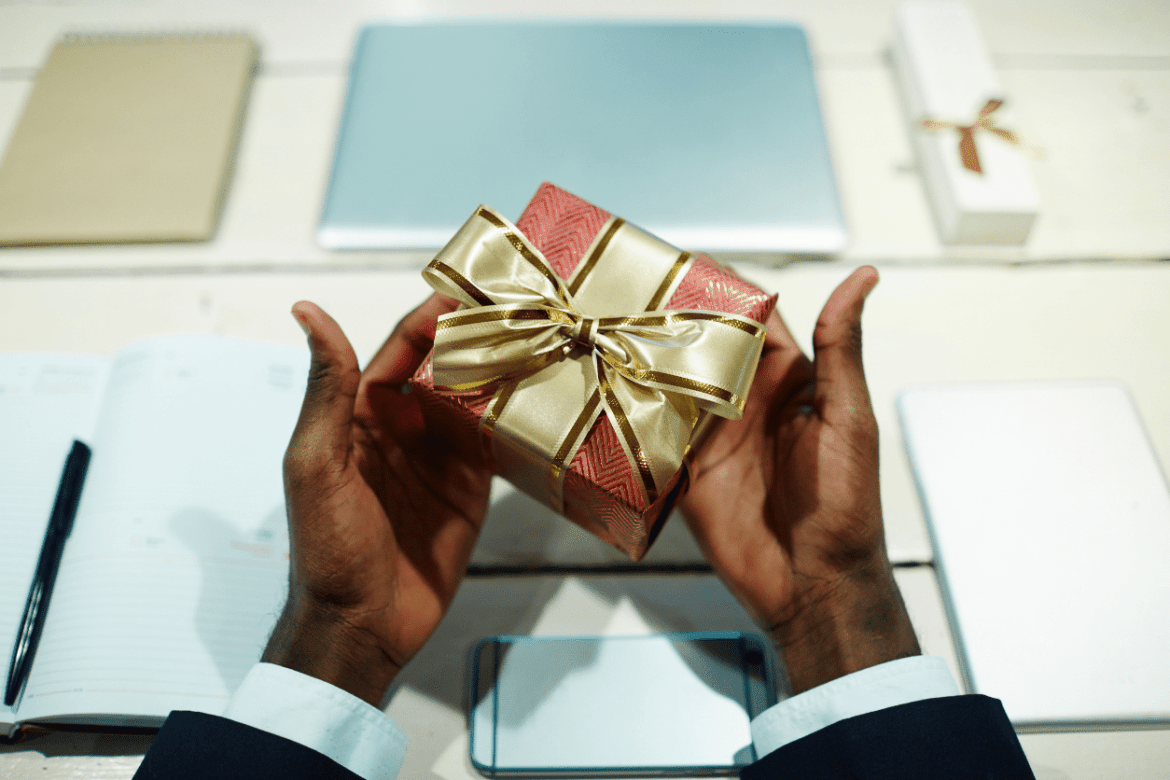 Man working at desk holding a business gift wrapped in a gold bow