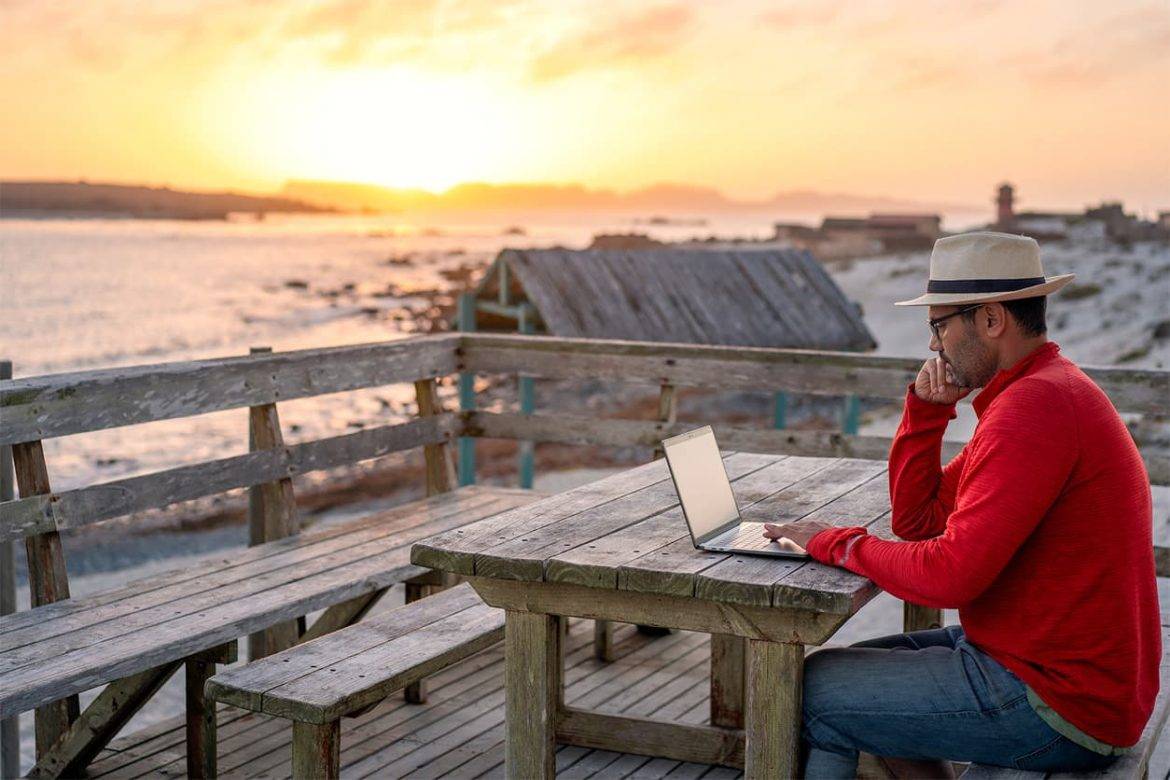 A man working on his laptop looking at the beach