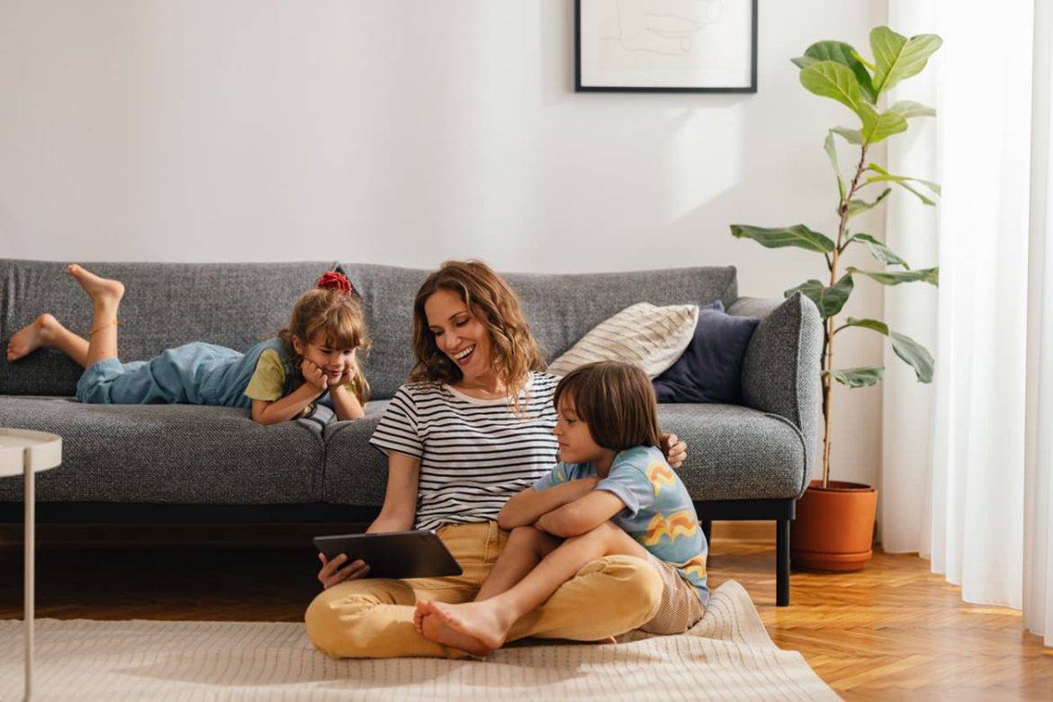 Mother Sits on the Floor and Watches Something on the Digital Tablet With Her Kids