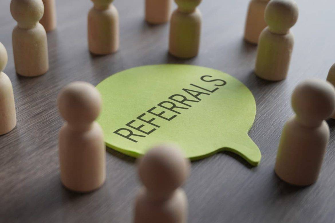 A group of wooden figurines surrounding a speech bubble with text REFERRALS